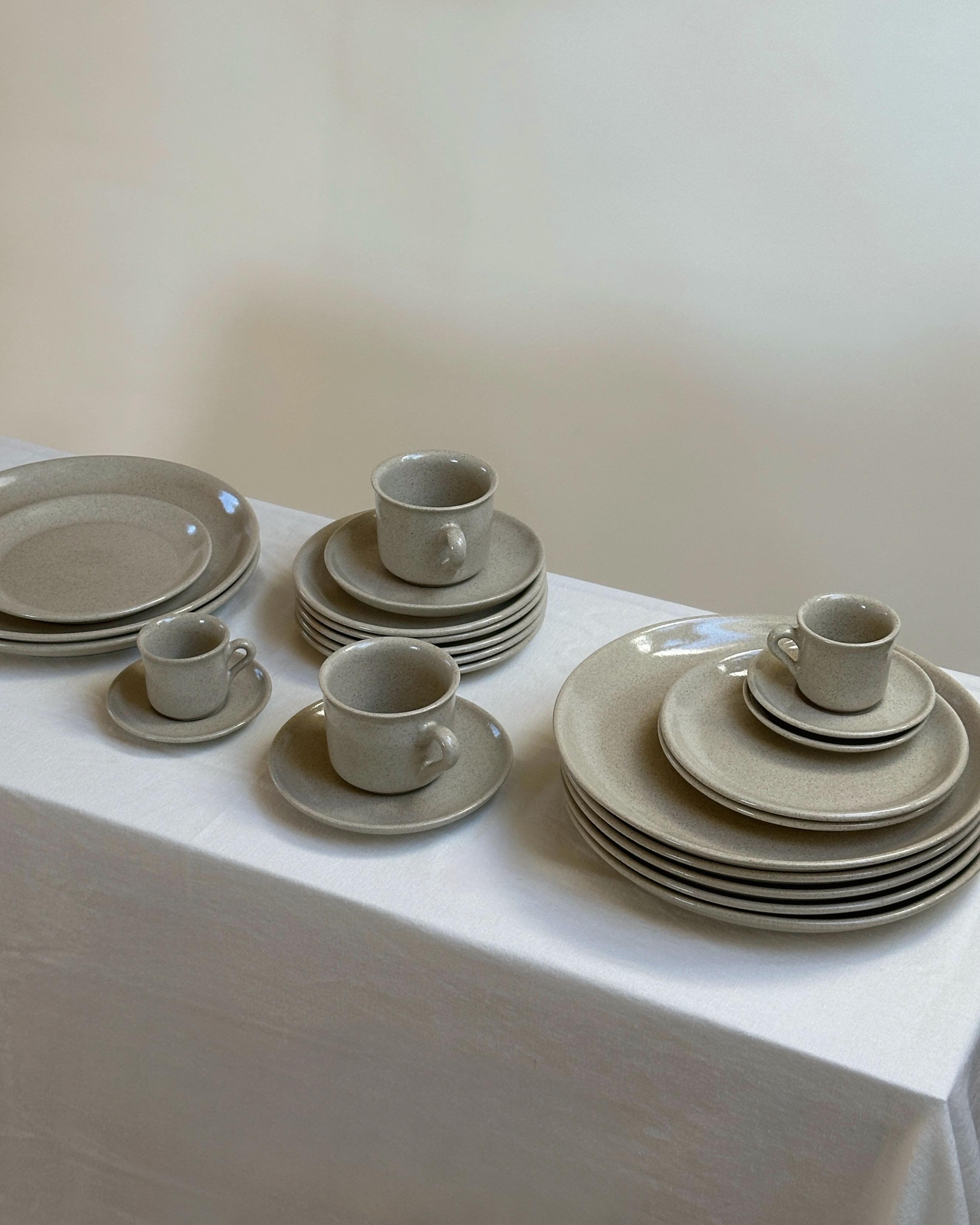 Steingut Geschirr gestapelt auf schmalem Regal mit weißer Tischdecke.