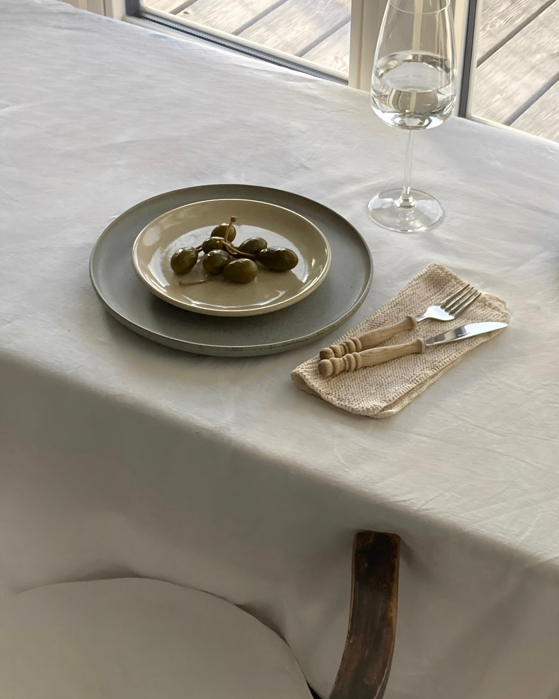 Großer blauer Keramikteller mit sandfarbenem Teller und Kapern auf Tisch mit weißer Tischdecke.