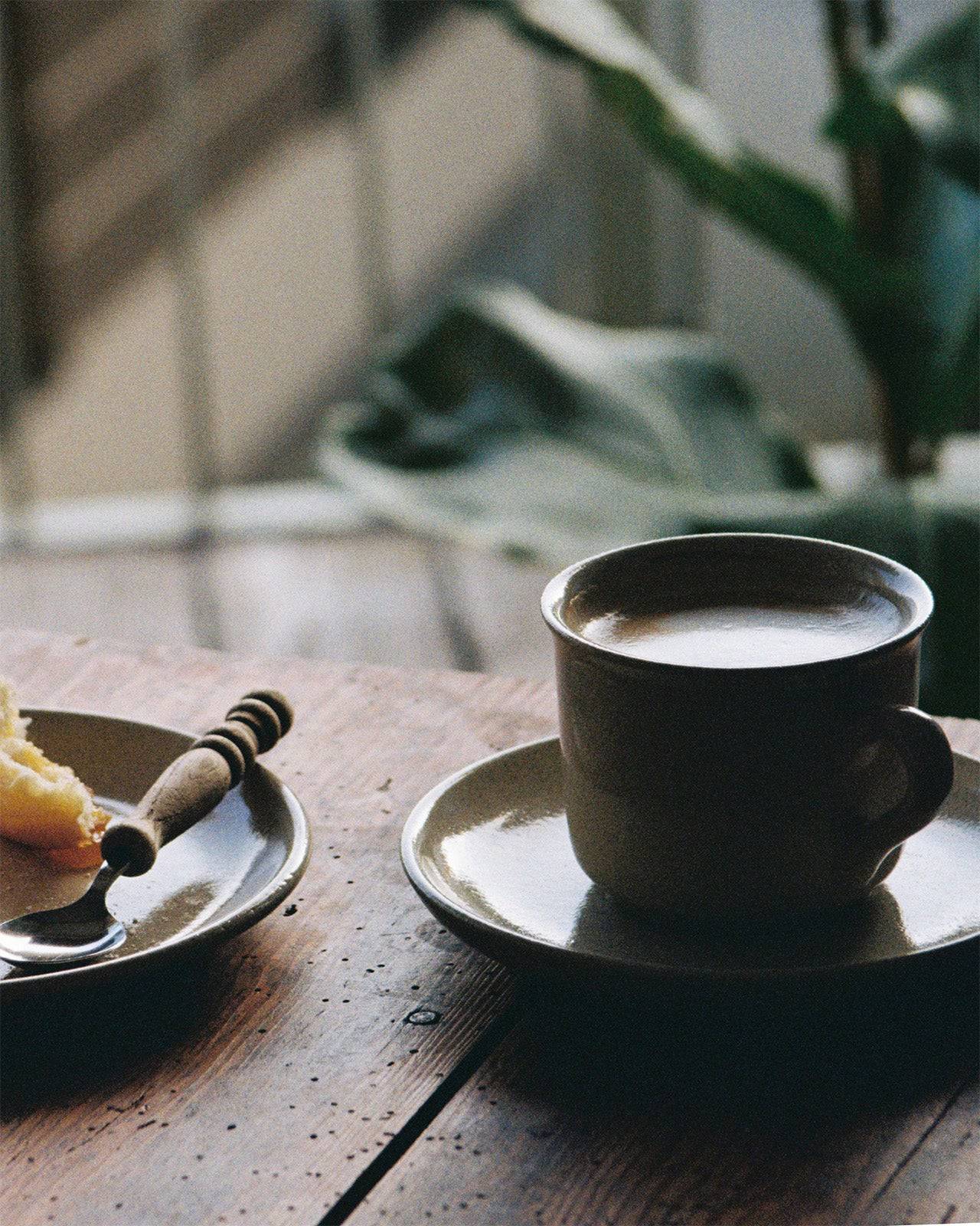 Analoge Fotografie von der Keramiktasse und dem kleinen Keramikteller aus der Viana-Kollektion auf Holztisch. 