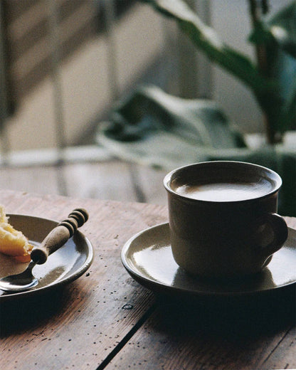 Analoge Fotografie von der Keramiktasse und dem kleinen Keramikteller aus der Viana-Kollektion auf Holztisch. 