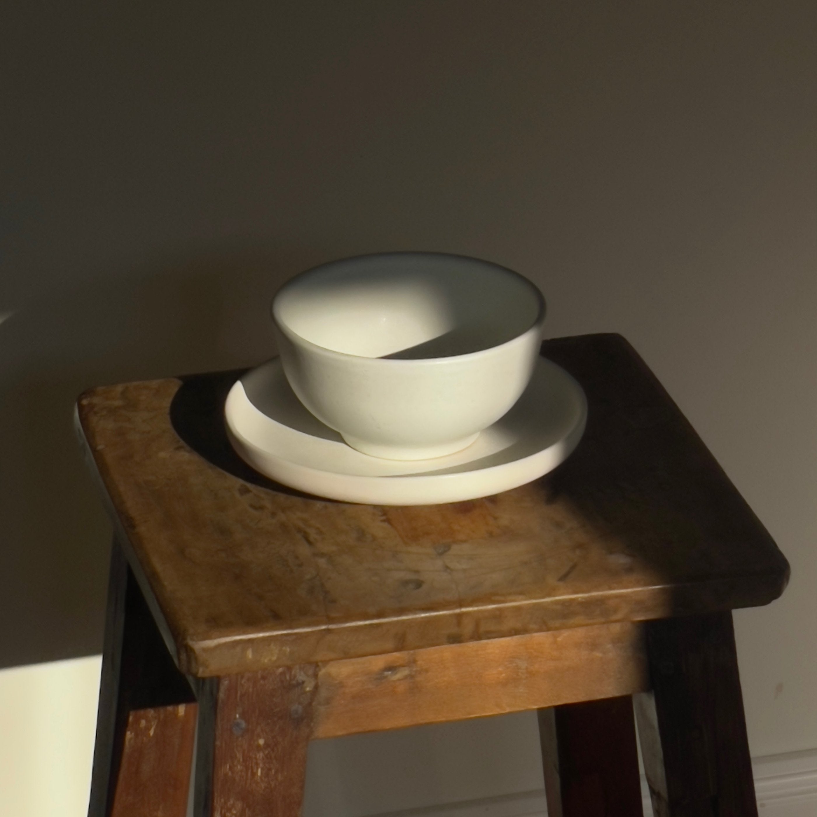 Weißer Teller mit kleiner Schüssel aus Steingut auf Holzhocker.