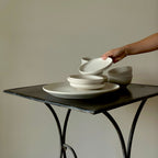 Weißes Geschirr aus Steinzeug gestapelt auf Metalltisch vor cremefarbener Wand