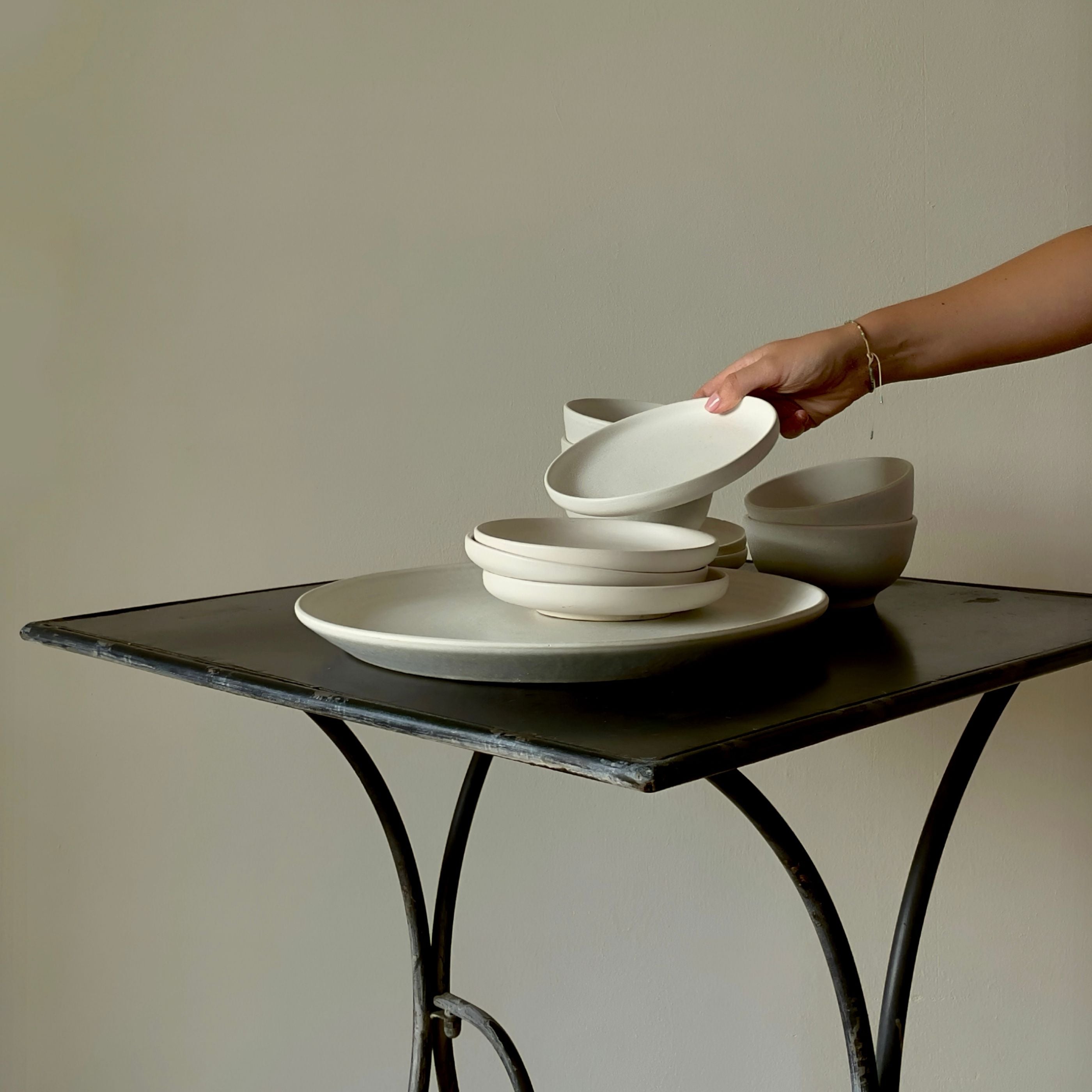 Weißes Geschirr aus Steinzeug gestapelt auf Metalltisch vor cremefarbener Wand