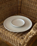 Großer weißer Servierteller aus Keramik mit kleinem weißen Keramikteller auf Korbstuhl.