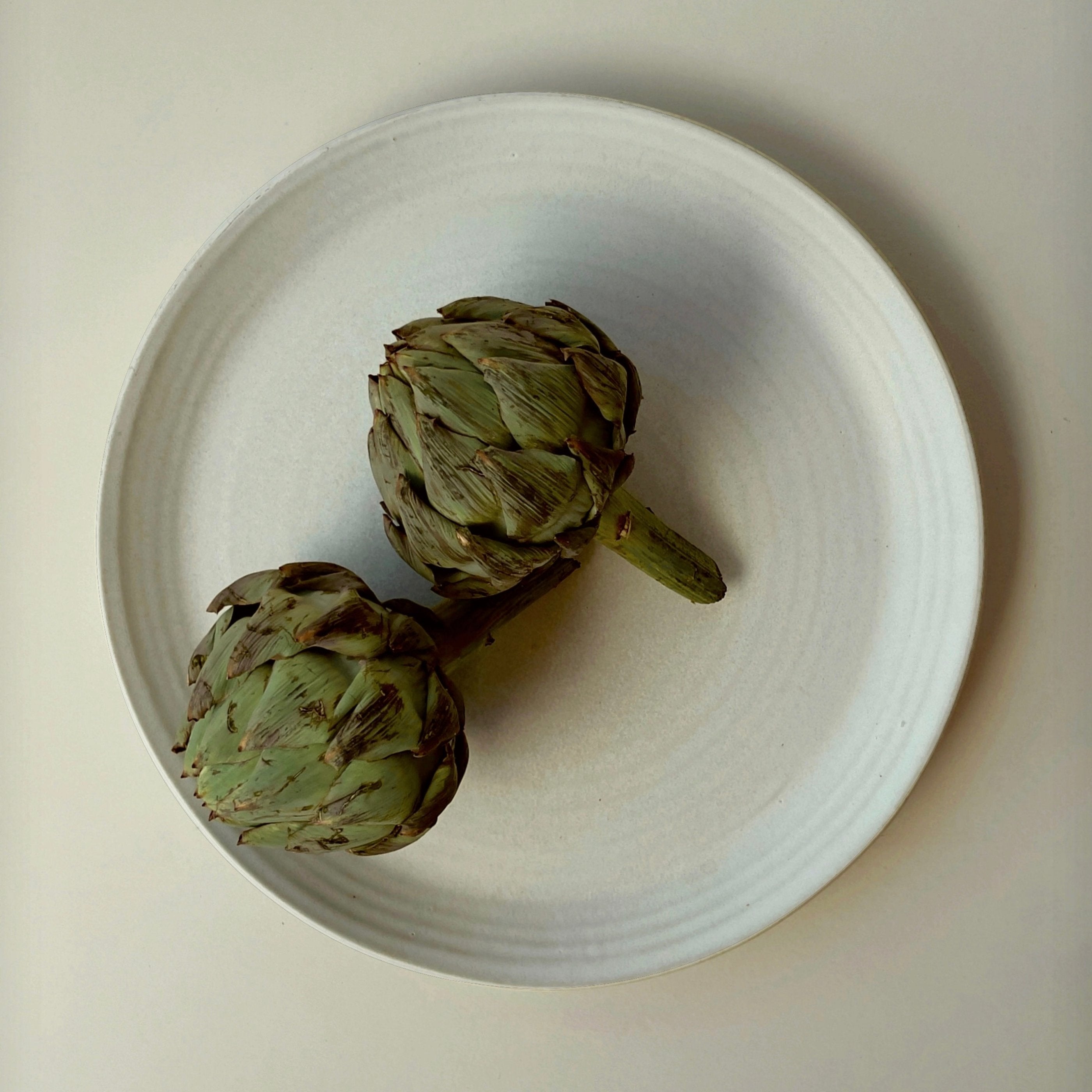 Weißer Servierteller aus Steingut mit zwei Artischocken