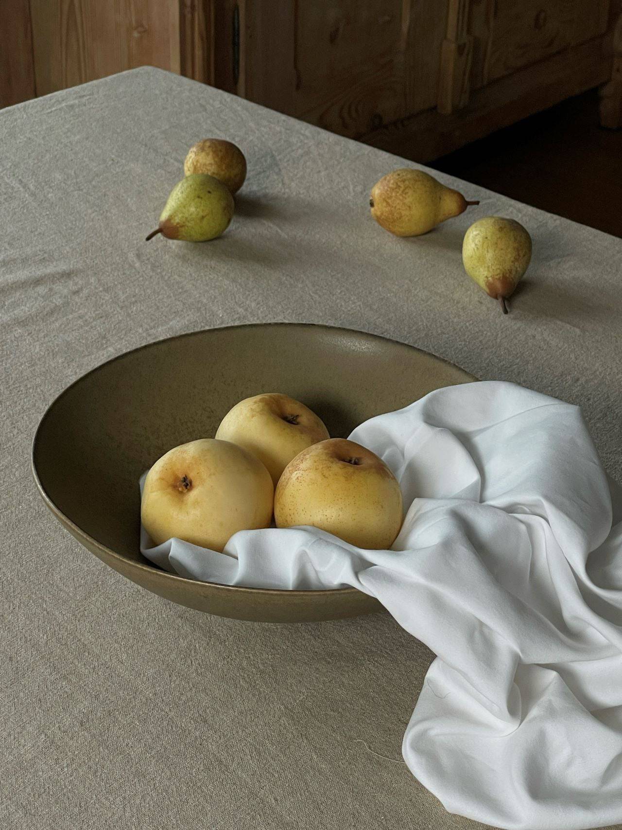 Obstschale Keramik große Keramikschüssel mit Birnen auf Tisch mit braungrauer Tischdecke.